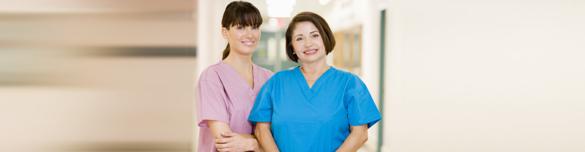Two Female Nurses Standing In A Hospital Corridor Smiling